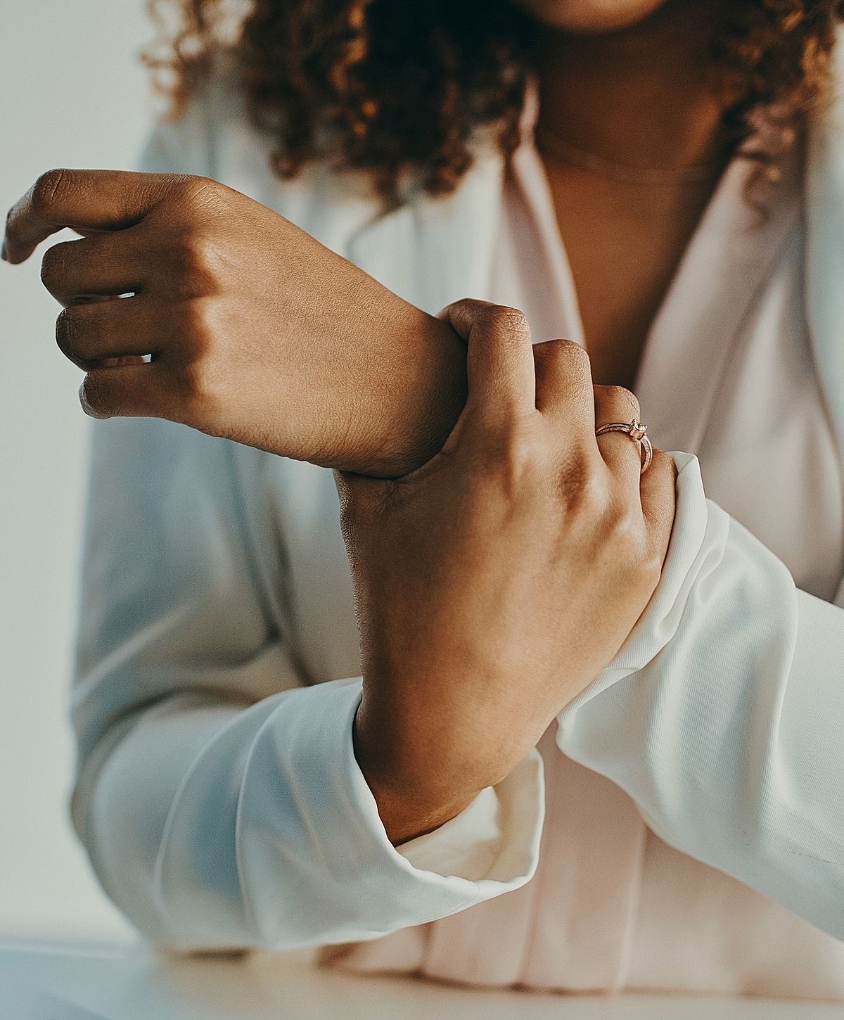 Hands adjusting sleeve with elegant rings visible.
