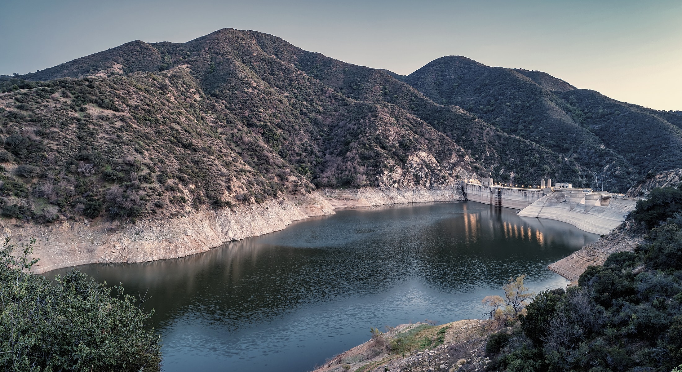 Dam surrounded by mountains and calm water.